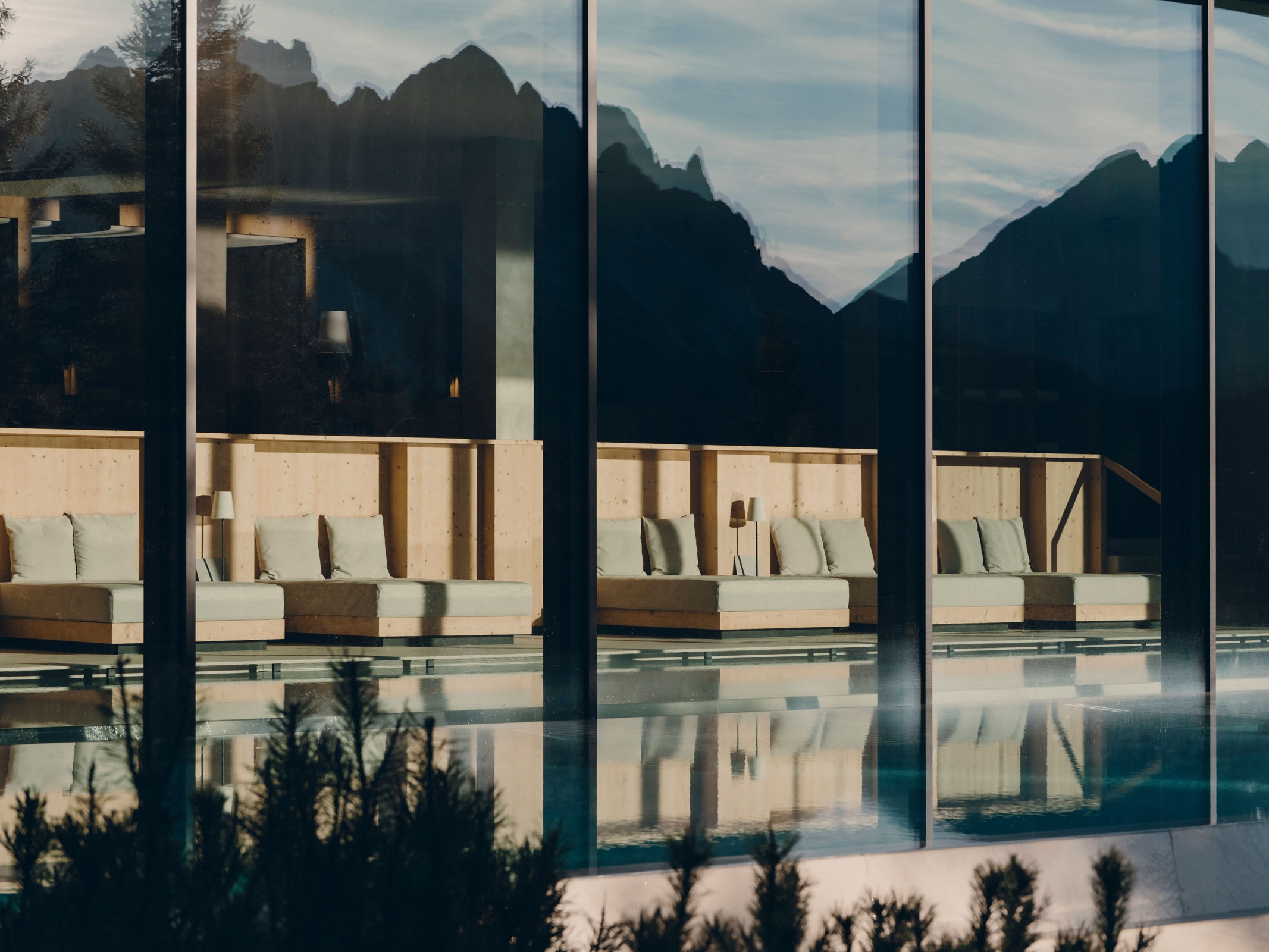 An outdoor infinity pool at FORESTIS reflects the hotel and forest, with the Dolomites rising behind it
