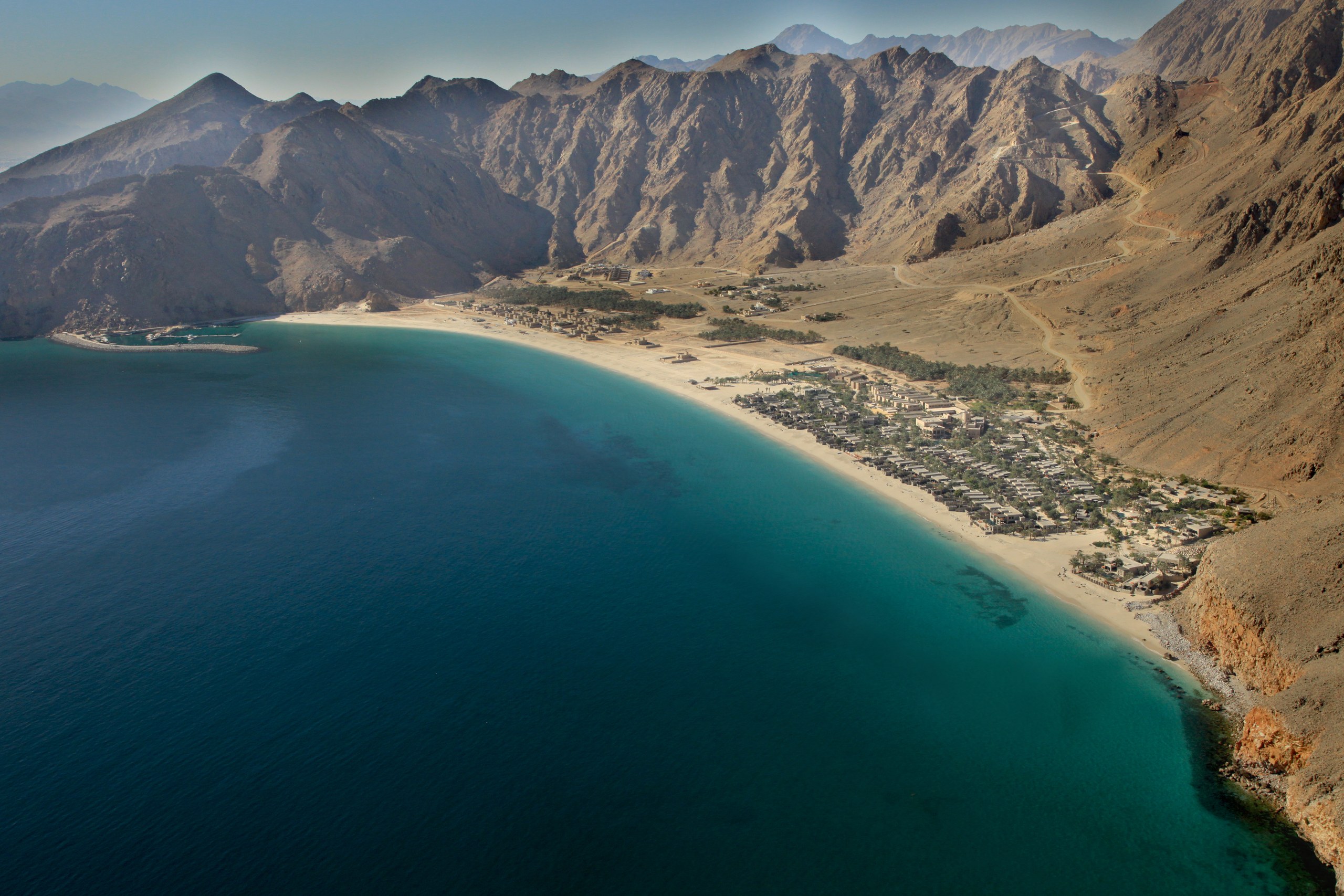 Aerial view of Six Senses Zighy Bay village and curved beach below the rugged Musandam mountains.