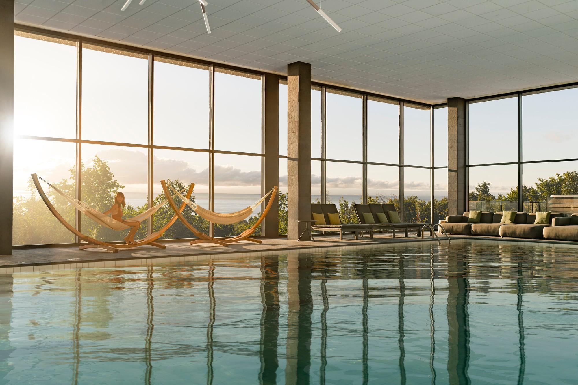 Indoor pool with floor-to-ceiling windows, hanging loungers and St. Lawrence River views at Club Med Québec Charlevoix