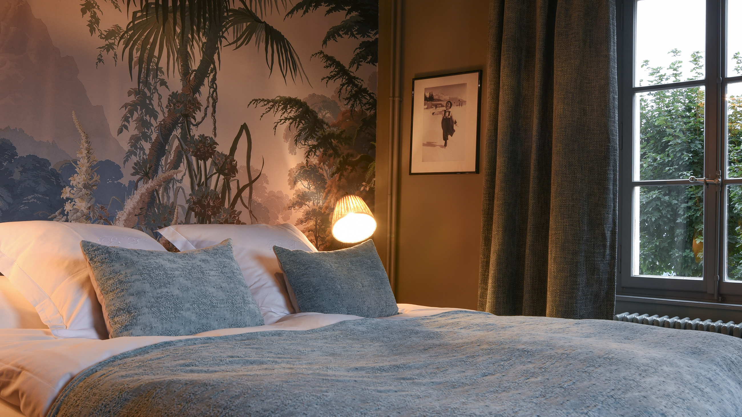 A Hotel Bella Tola suite with a painted mountain-forest mural and soft blue linens, St-Luc, Switzerland