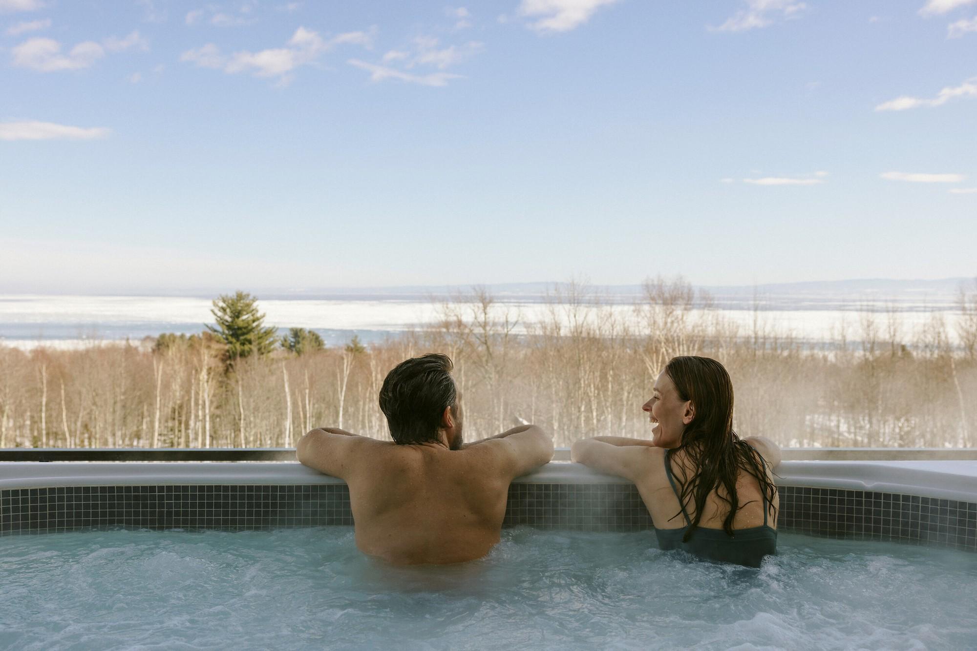Guests in the outdoor hot tub overlooking snowy forest and the St. Lawrence River at Club Med Québec Charlevoix