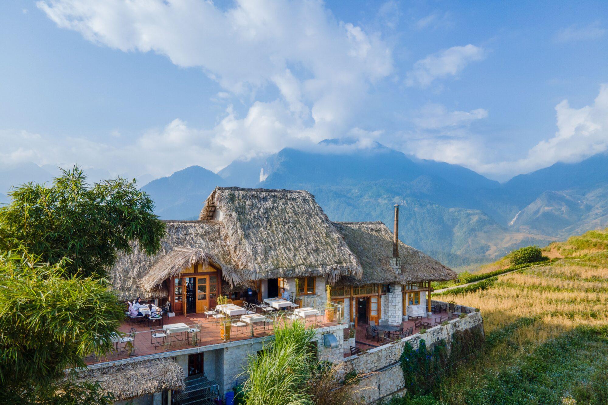 Thatched stone cottage exterior beside golden rice terraces, Topas Ecolodge, Sapa, Vietnam