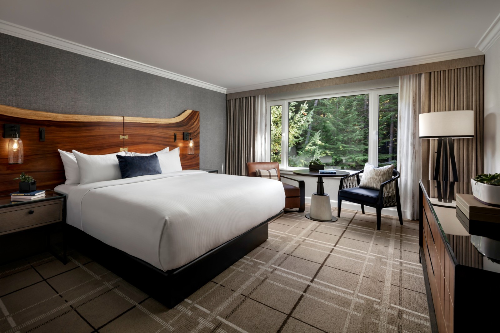 King-bed guest room with wooden headboard and a large window overlooking trees at Fairmont Chateau Whistler, British Columbia
