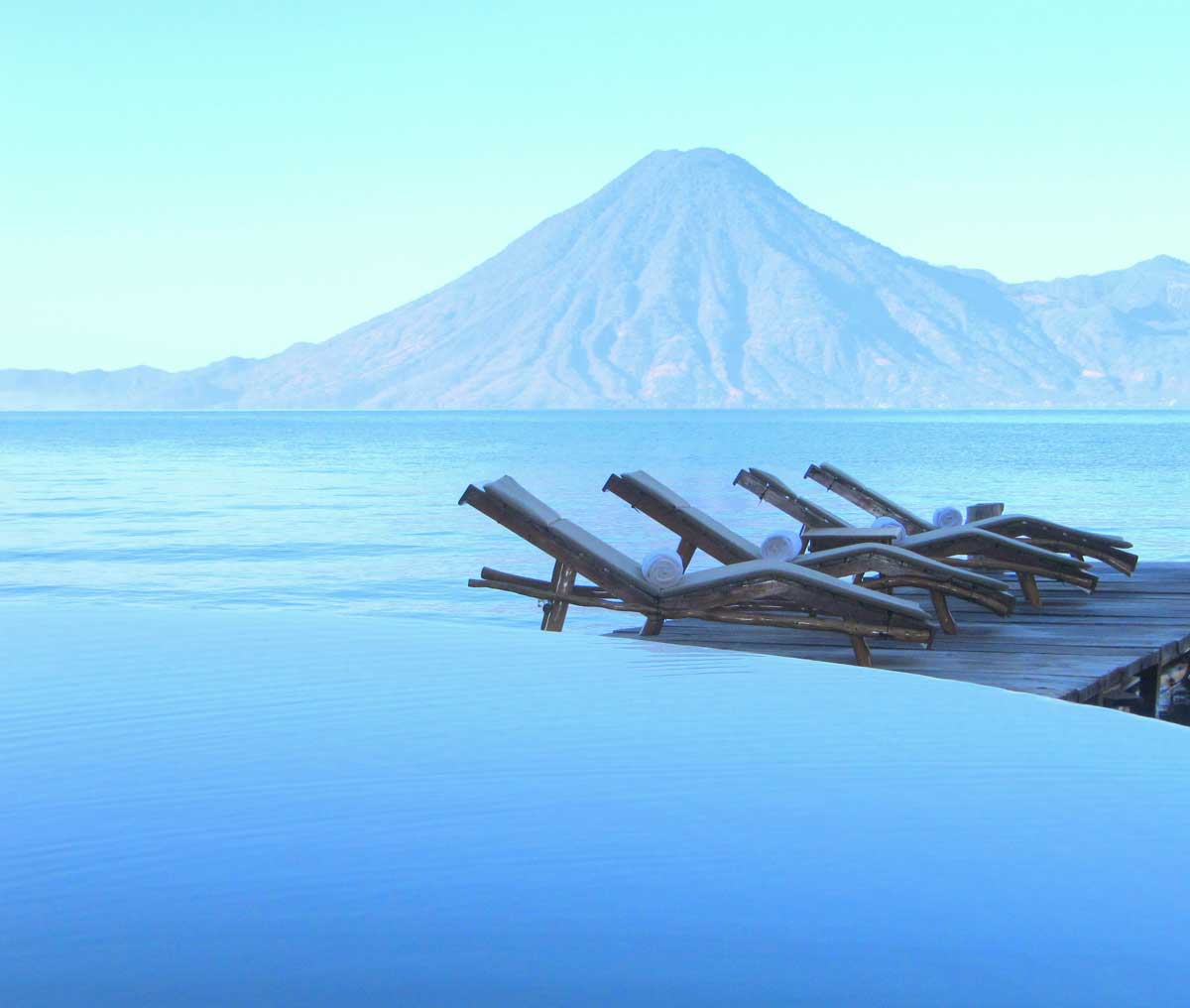 Infinity pool and wooden loungers facing a volcano, Laguna Lodge, Lake Atitlán, Guatemala