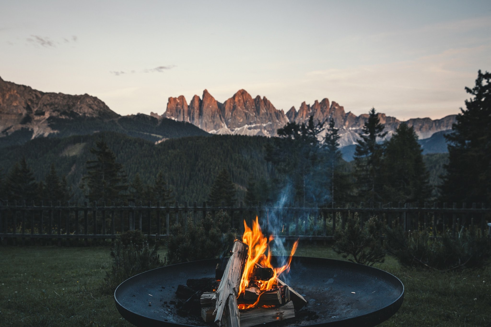 An outdoor fire pit at FORESTIS with mountain peaks visible beyond the trees, Dolomites, Italy