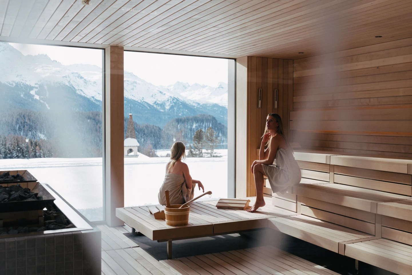 Guests in the timber sauna facing snowy mountains through panoramic windows, Suvretta House, St. Moritz, Switzerland