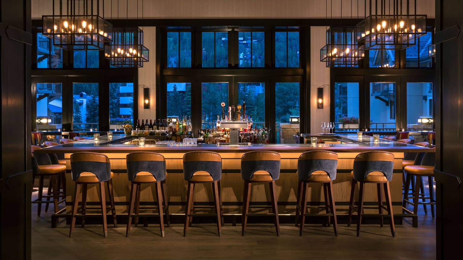 The Remedy bar with wood stools and mountain-view windows at dusk at Four Seasons Resort Vail.