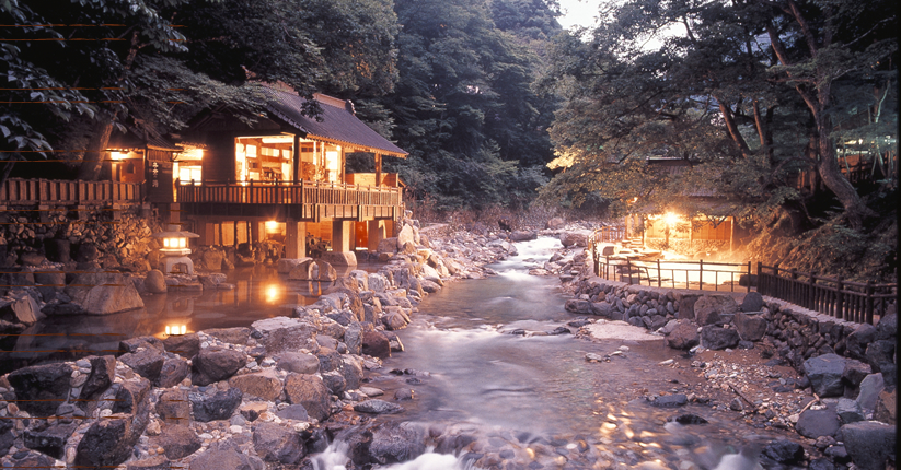 Illuminated riverside buildings and rock-edged bathing areas at dusk at Takaragawa Onsen Osenkaku, Gunma, Japan