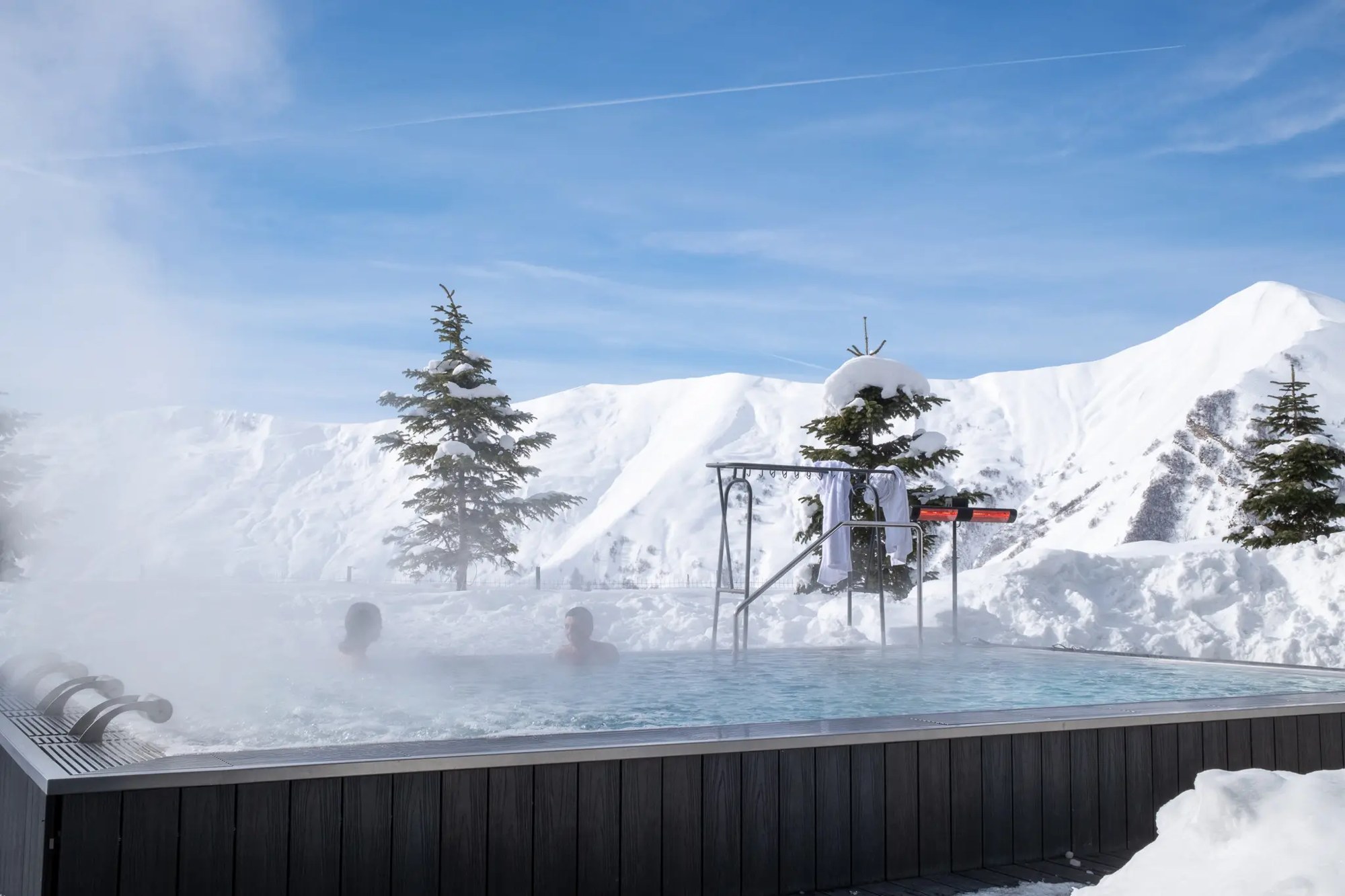 Steaming outdoor hot tub beside snow-covered trees at Gudauri Lodge
