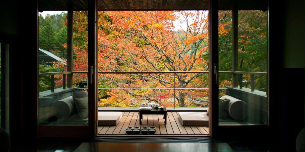 Open terrace and low seating framed by dark sliding doors, overlooking vivid orange autumn foliage, Hoshinoya Karuizawa
