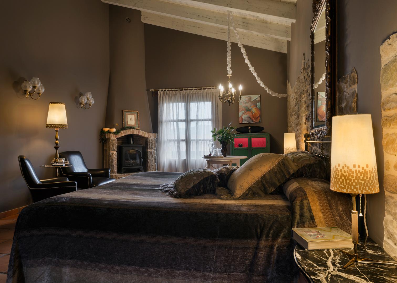 Guest room with dark bedding, exposed stone wall and a fireplace at Hotel Barosse, Jaca, Spain