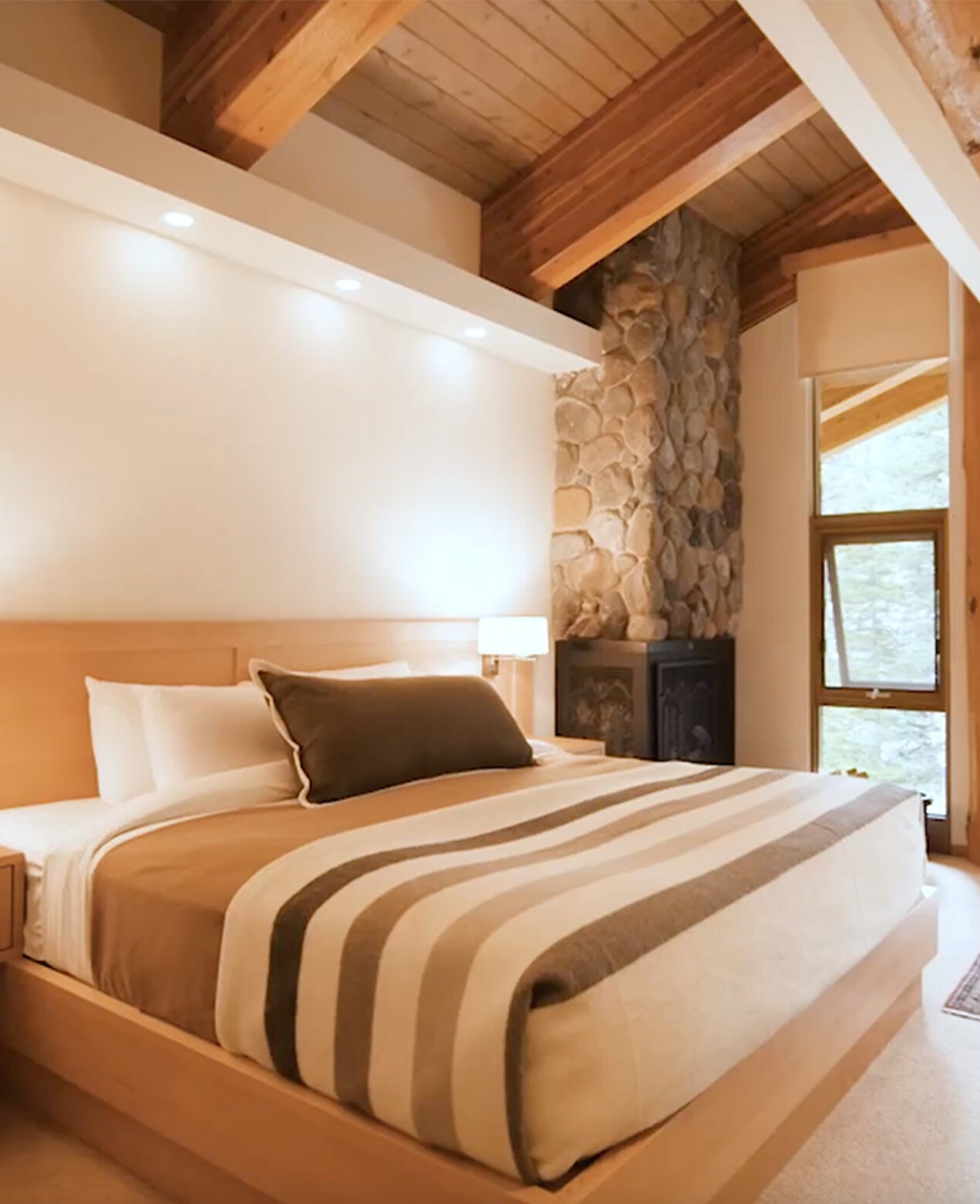 Rustic guest bedroom with timber beams and stone fireplace at Moraine Lake Lodge, Moraine Lake, Canada