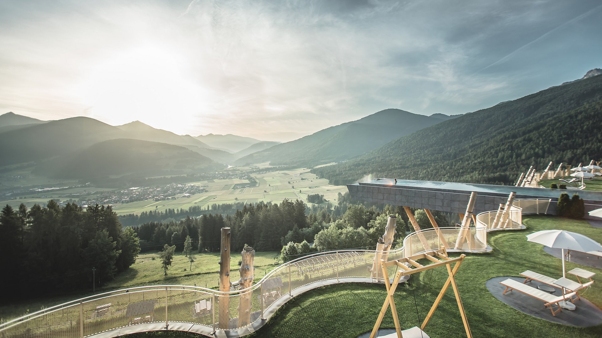 Outdoor play area overlooking a green mountain valley at Alpin Panorama Hotel Hubertus, Olang, Italy