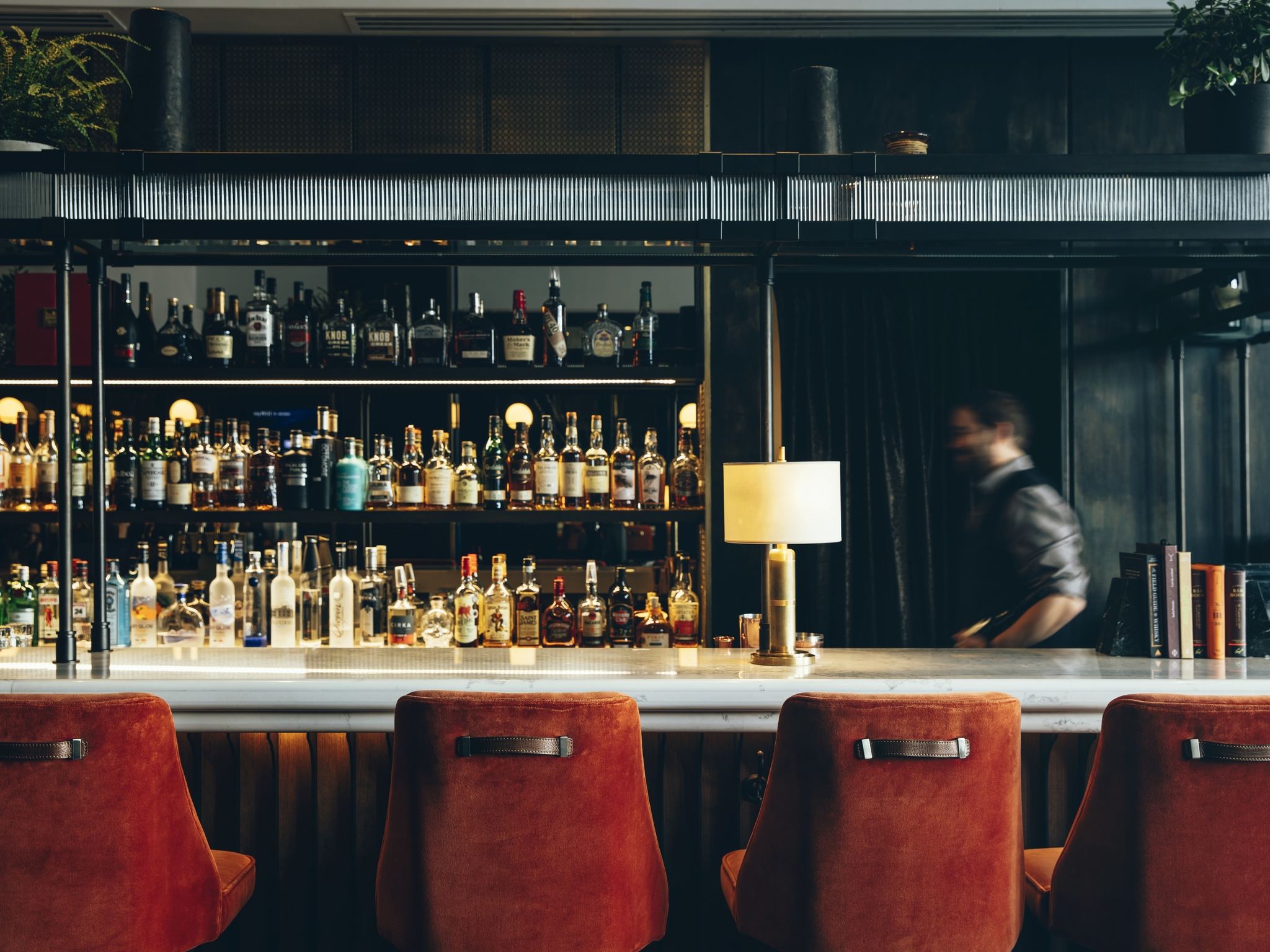 Bar at Fairmont Tremblant with red upholstered stools and illuminated bottle shelves.