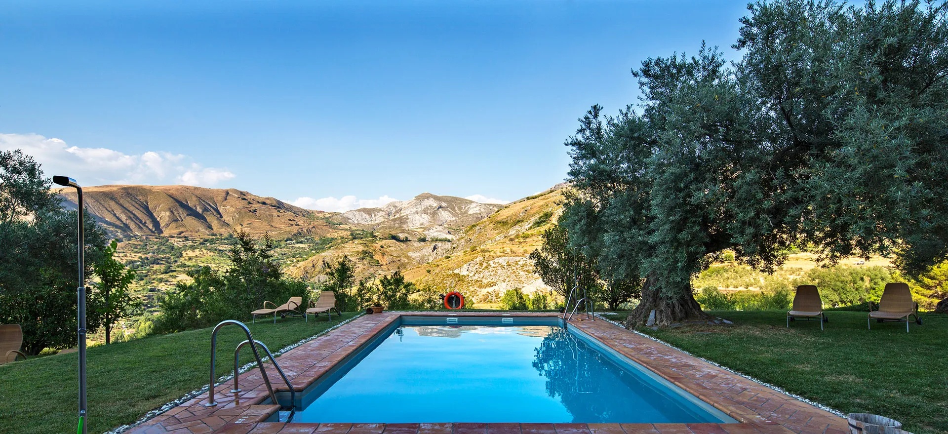 Outdoor swimming pool framed by trees and hills at La Almunia del Valle, Monachil, Spain