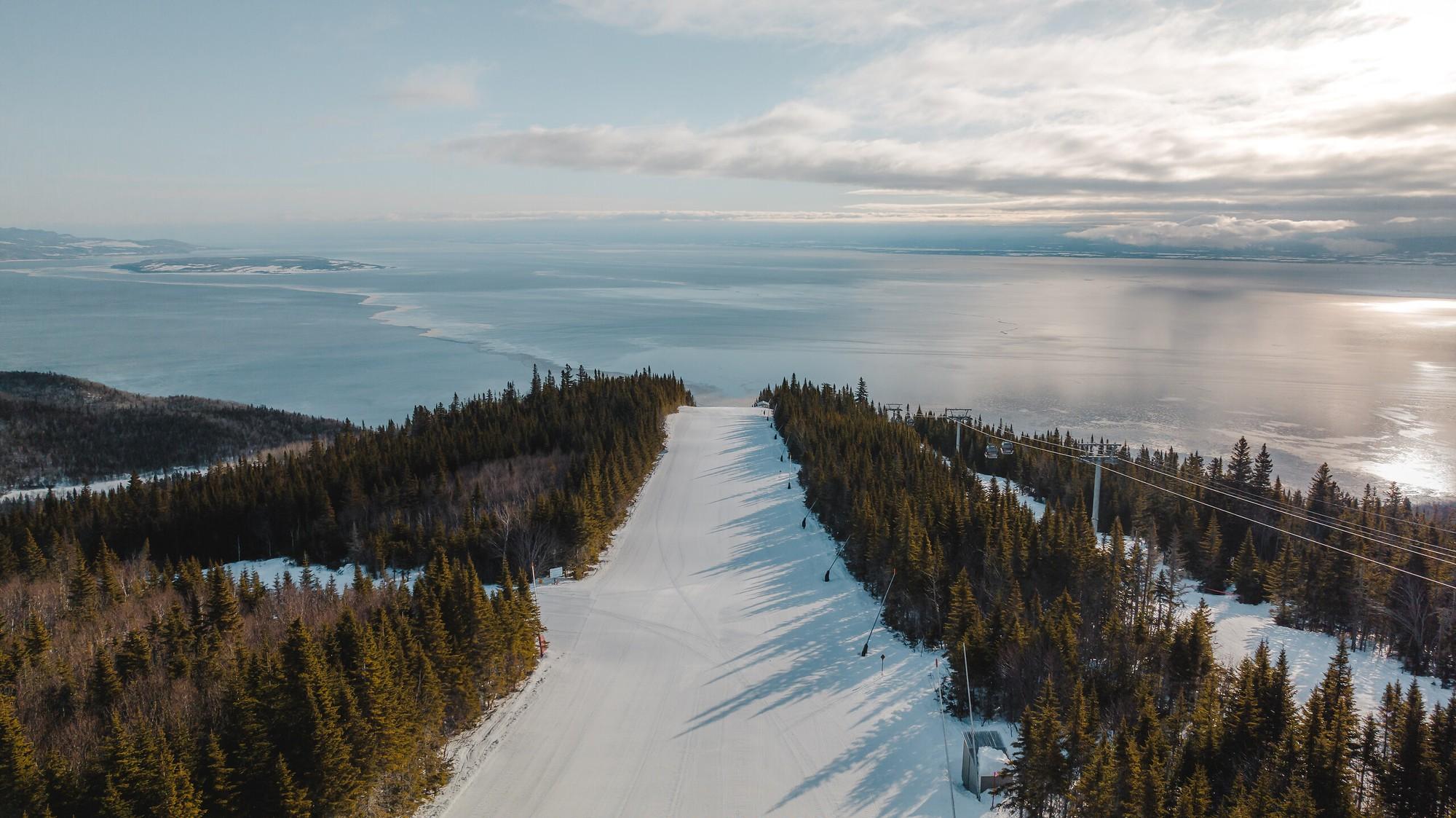 Snow-covered Le Massif ski slopes descending through forest towards the St. Lawrence River, Club Med Québec Charlevoix