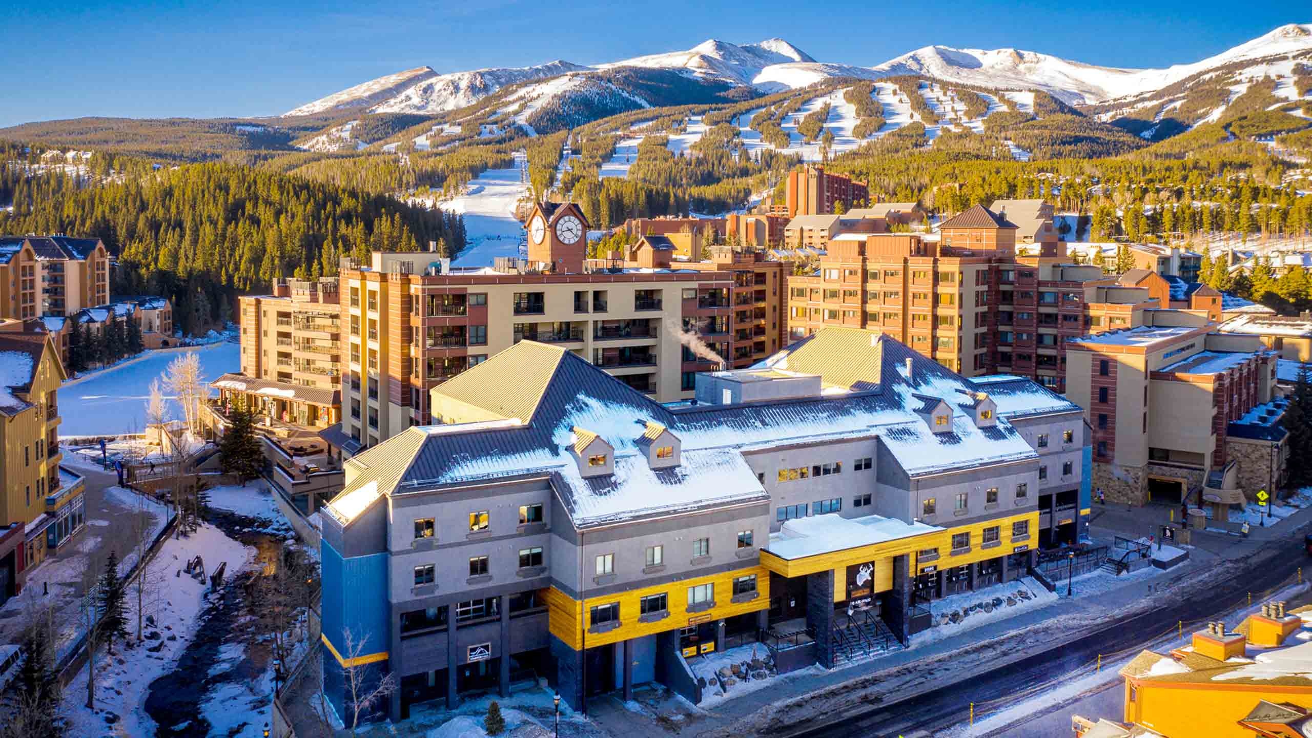 Aerial winter view of Gravity Haus Breckenridge with snowy roofs and the ski mountain behind it.