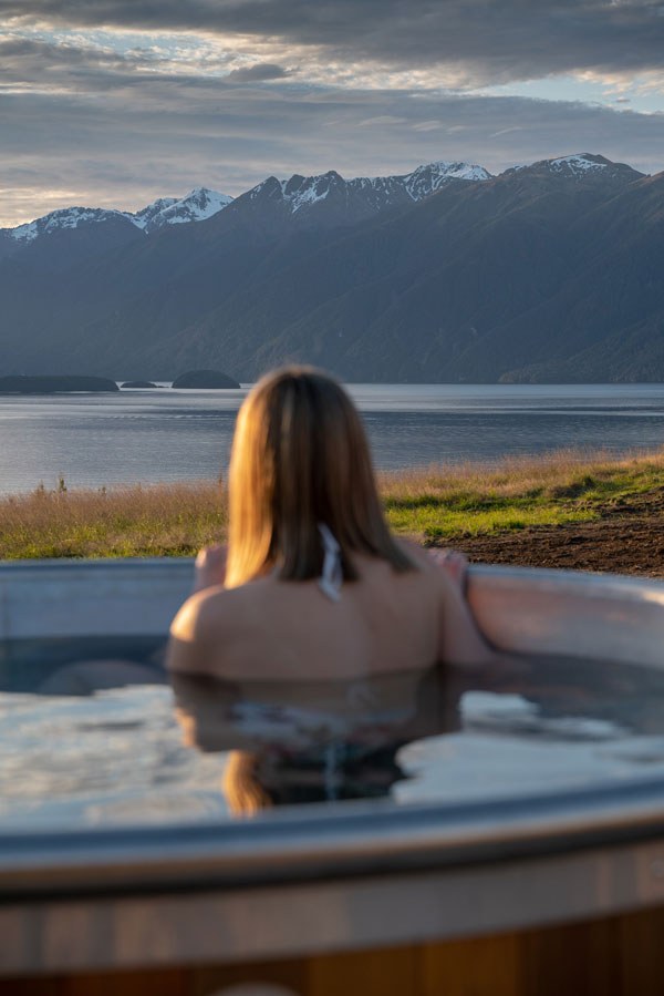 Guest in an outdoor hot tub overlooking Lake Te Anau at Fiordland Lodge