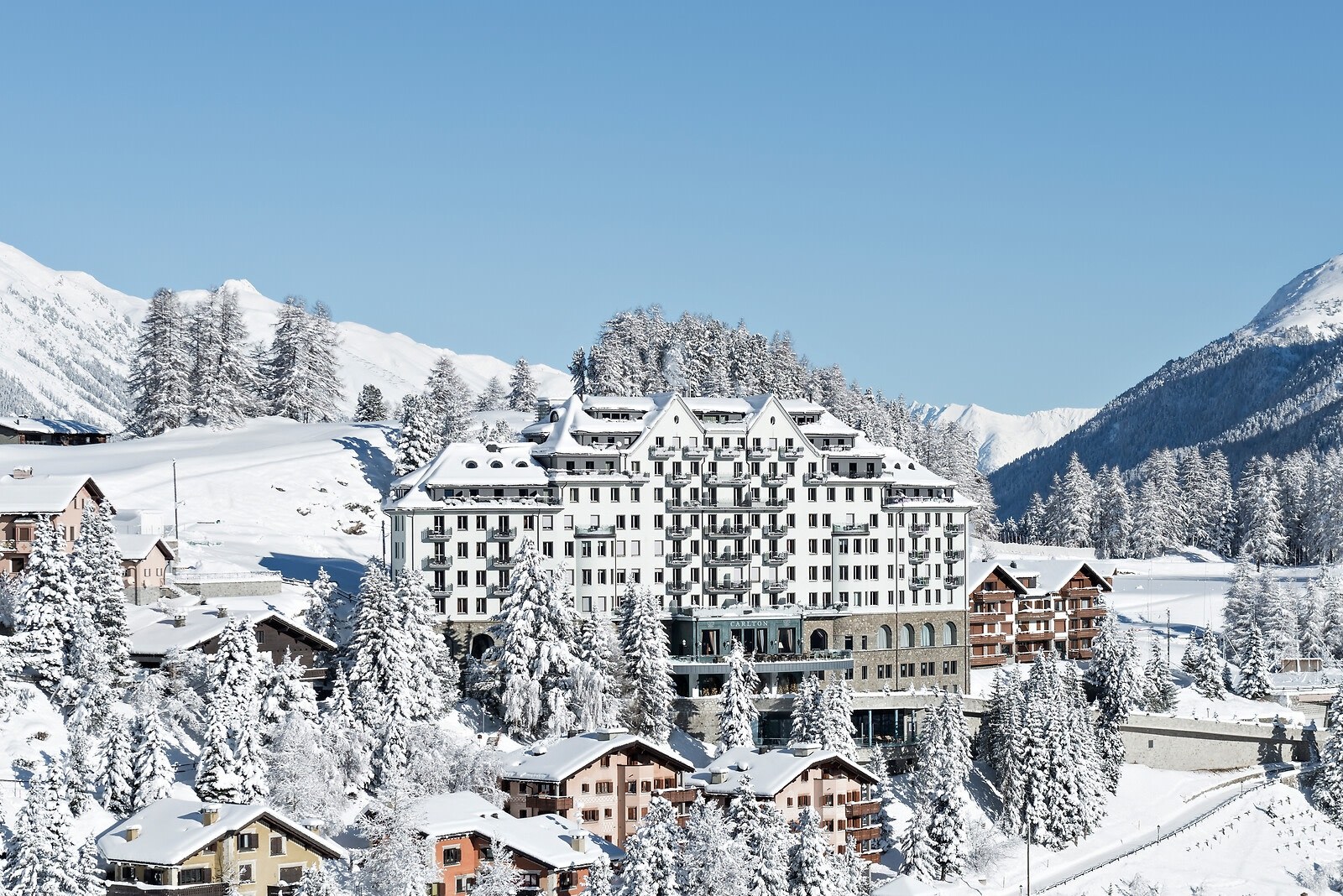Grand hotel facade and surrounding chalets beneath snowy Engadine mountains, Carlton Hotel St. Moritz, St. Moritz, Switzerland