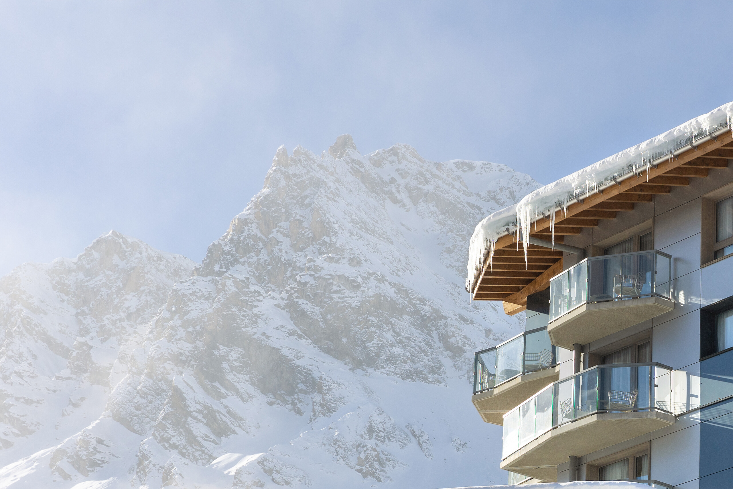 Snow-covered balconies beneath a timber roof at Club Med Tignes, with snowy Alpine peaks behind