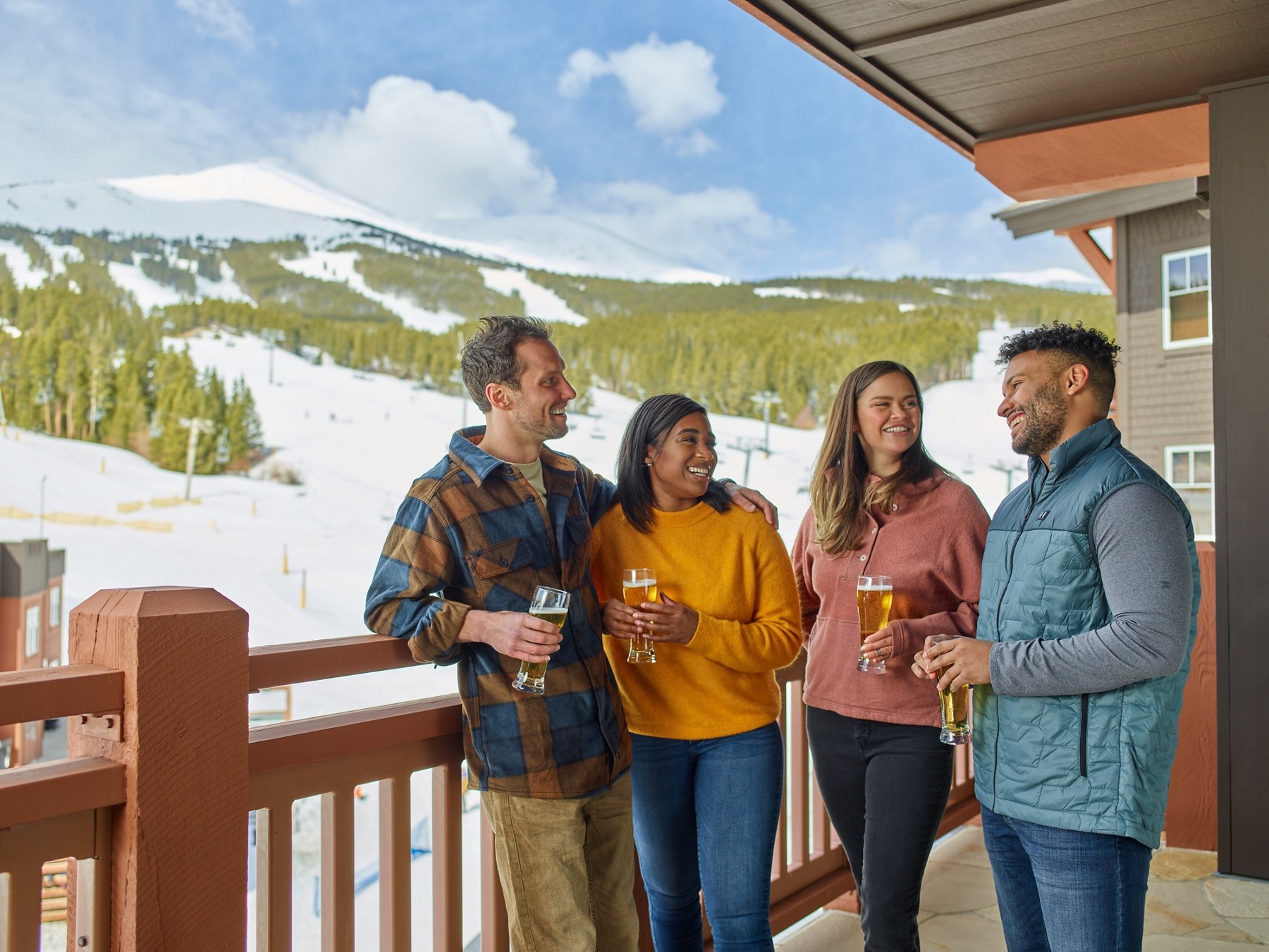Four friends sharing drinks on a One Ski Hill Place balcony overlooking snowy ski slopes.
