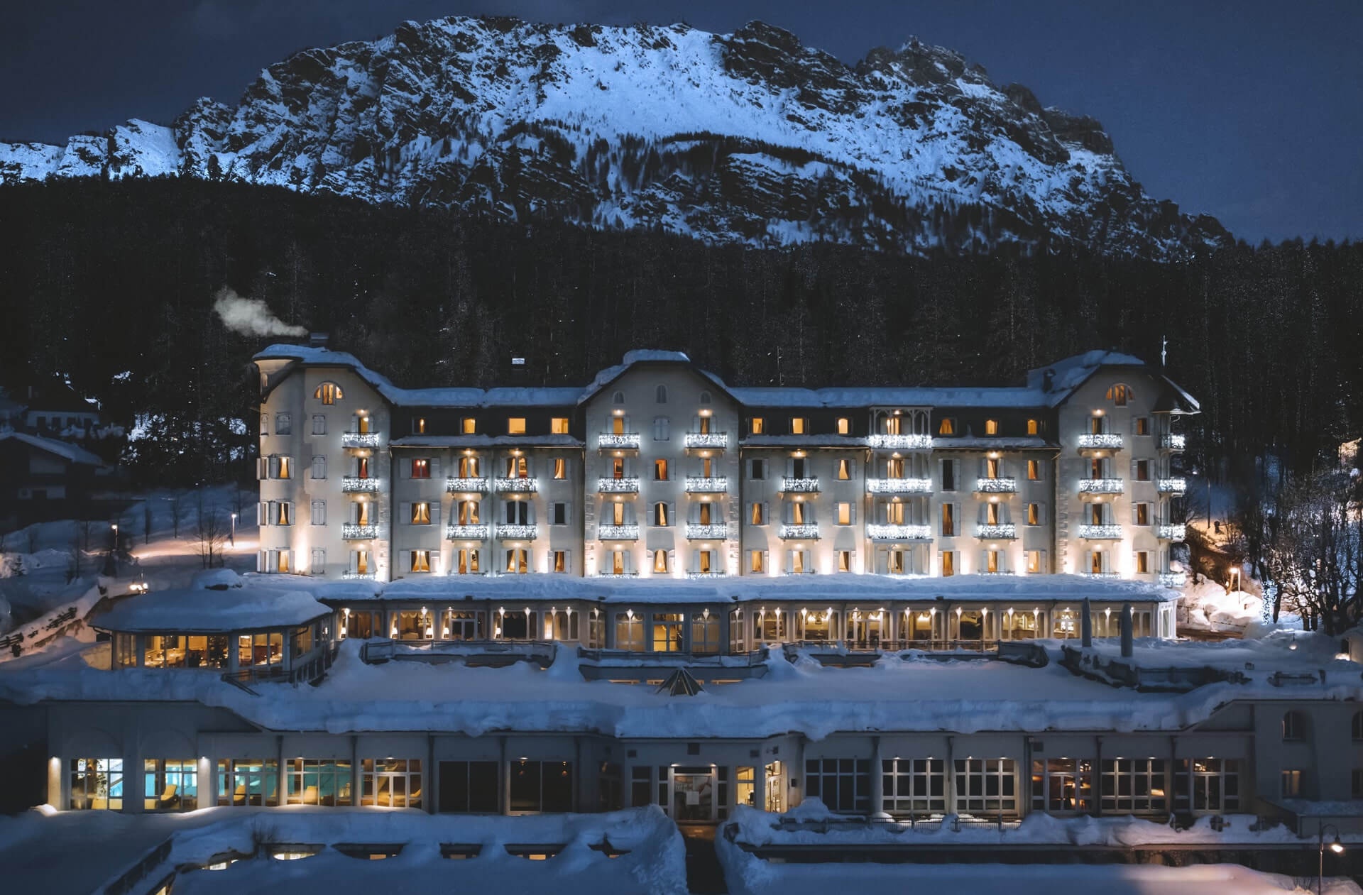 Historic hotel illuminated in winter beneath snow-covered mountains at Mandarin Oriental Cristallo, Cortina