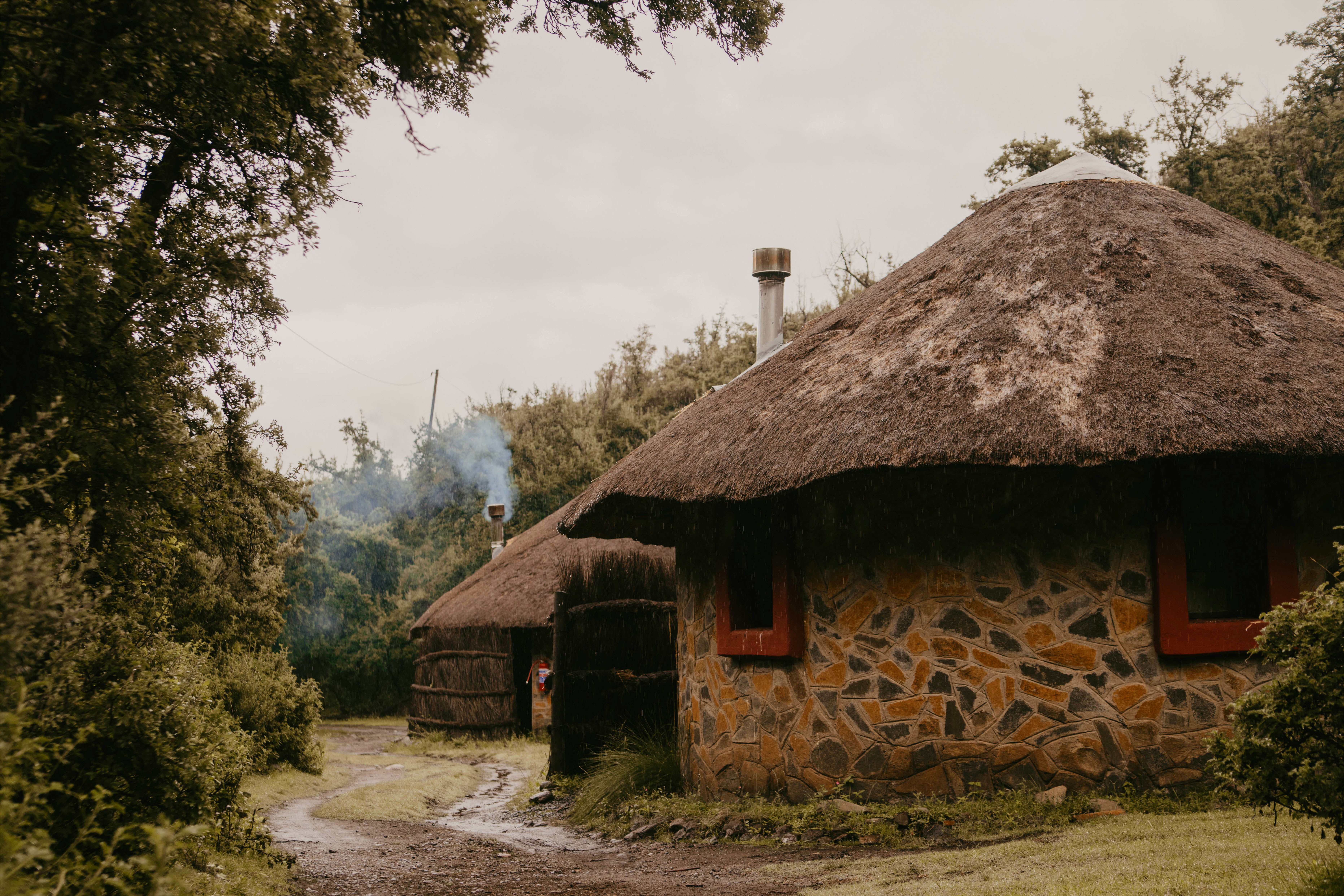 Stone and thatch chalet exterior among trees, Maliba Mountain Lodge, Ts’ehlanyane National Park, Lesotho