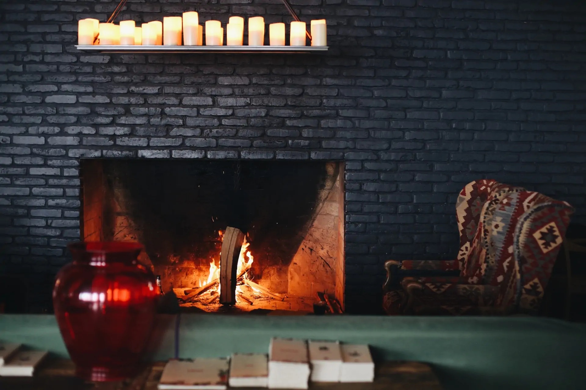 Fire burning in a dark brick fireplace beside patterned seating at Rooms Hotel Kazbegi, Georgia