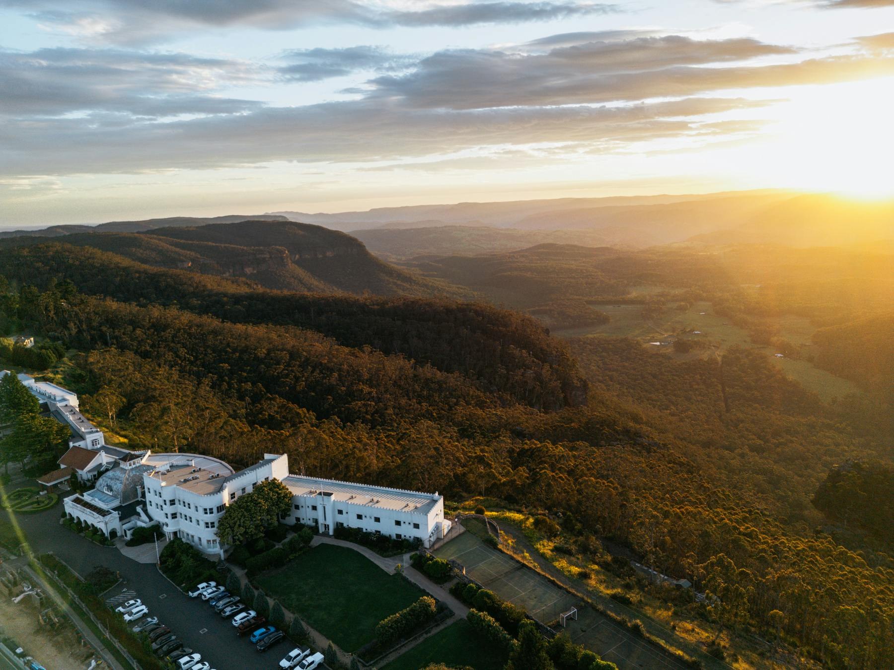 Aerial view of Hydro Majestic Hotel above the forested Megalong Valley at sunset