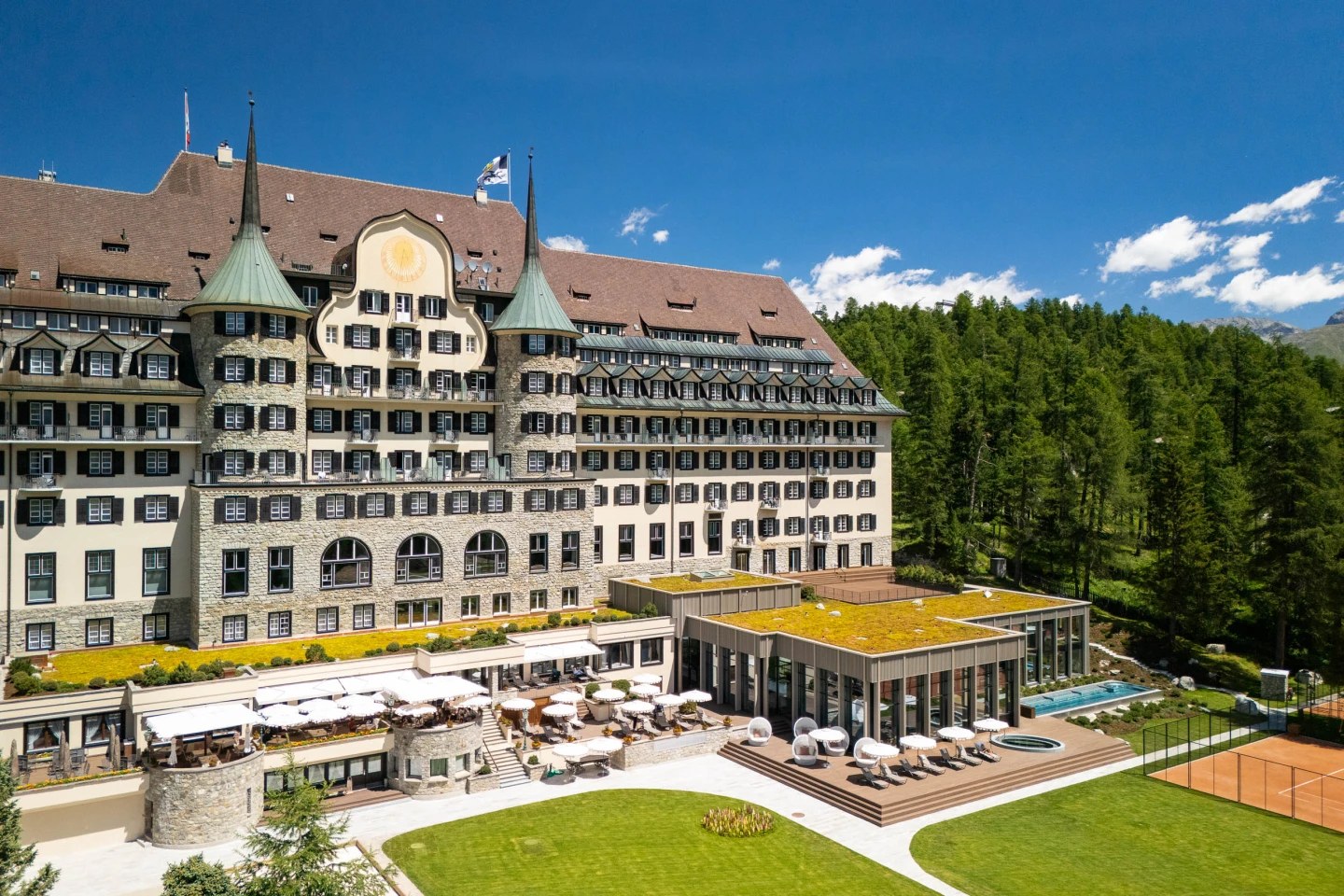 Grand hotel facade and garden terraces beside the outdoor pool, surrounded by forest in summer, Suvretta House, St. Moritz, Switzerland