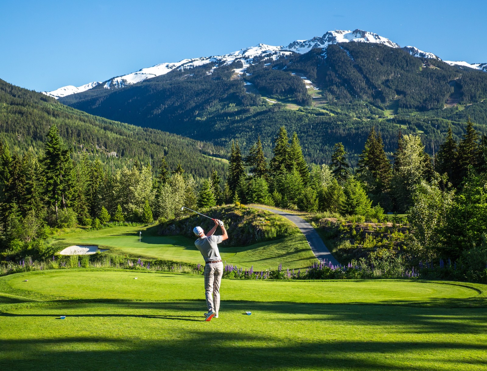 Golfer mid-swing on a mountain-framed fairway at Fairmont Chateau Whistler Golf Club, British Columbia, Canada