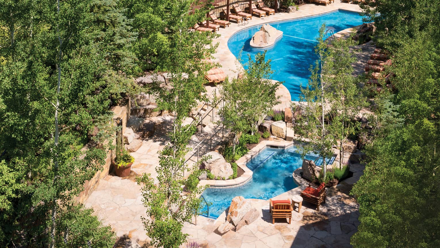 Aerial view of winding outdoor swimming pool, deck with lounge chairs surrounded by trees, Four Seasons Resort Jackson Hole, Teton Village, USA