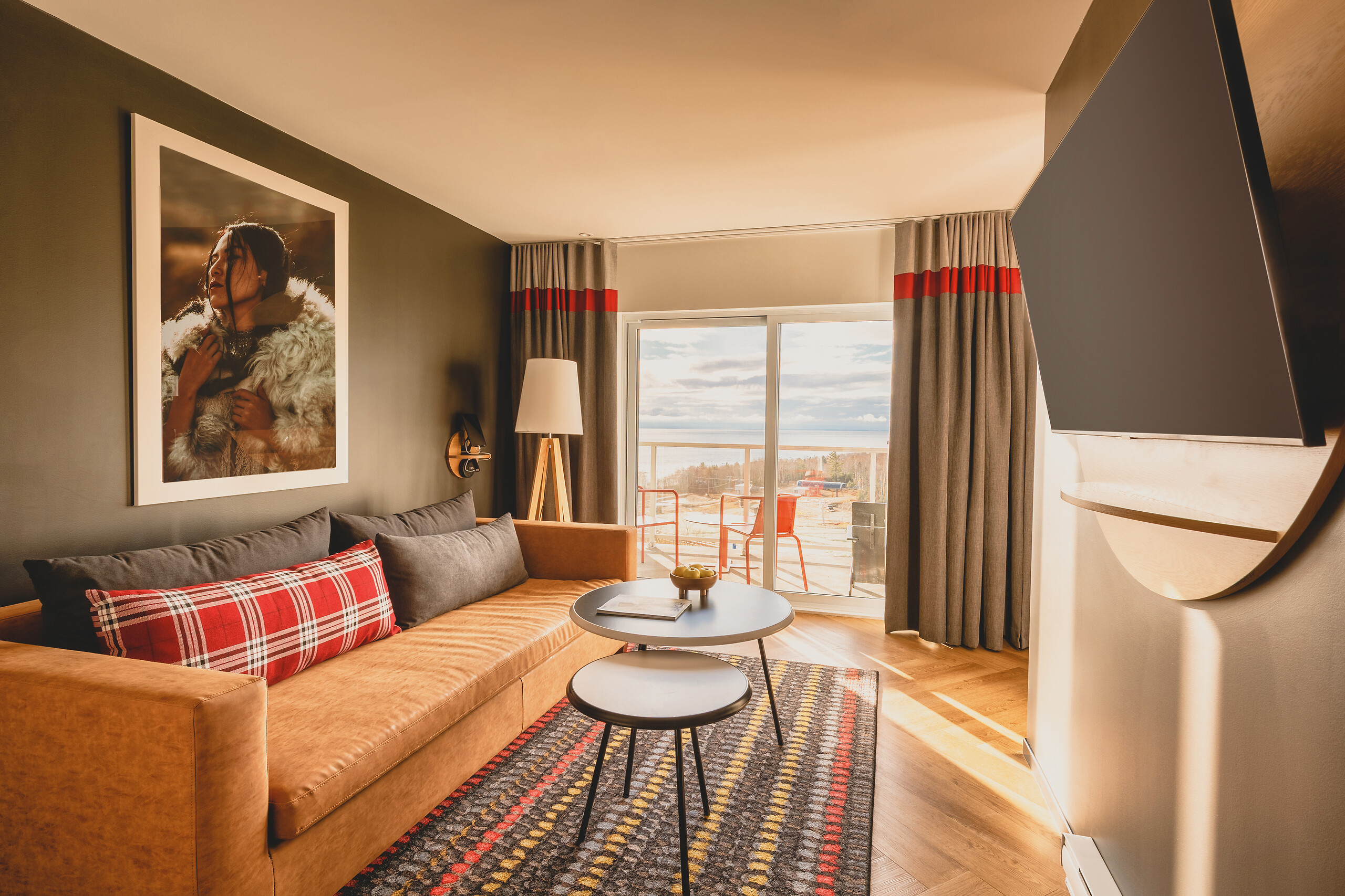 Exclusive Collection suite lounge with a tan sofa, round tables and balcony doors at Club Med Québec Charlevoix