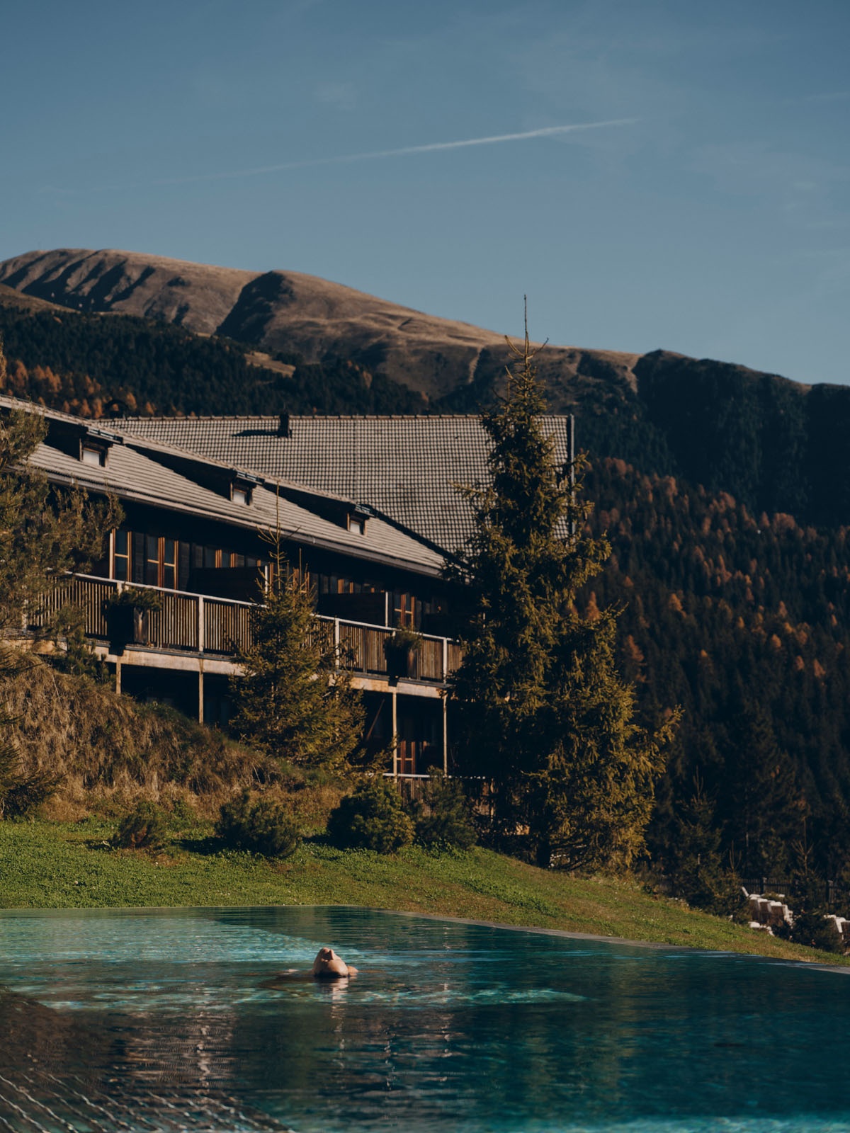 Hotel building viewed among the trees with the Dolomites in the background at FORESTIS, Dolomites, Italy