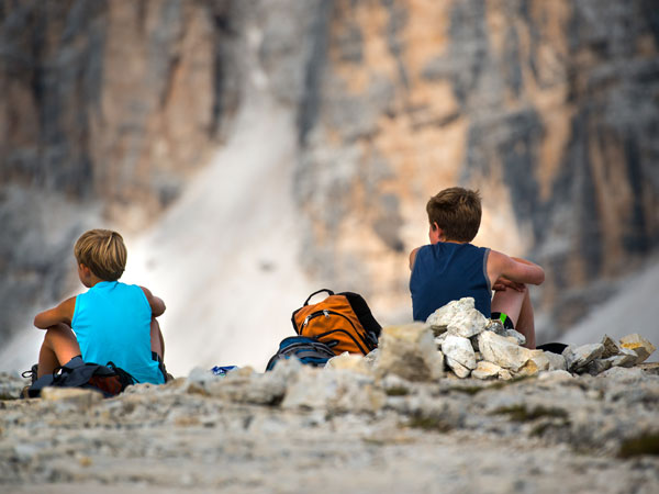 Two hikers sitting on rocks overlooking steep mountain cliffs at Rifugio Lagazuoi, Dolomites, Italy