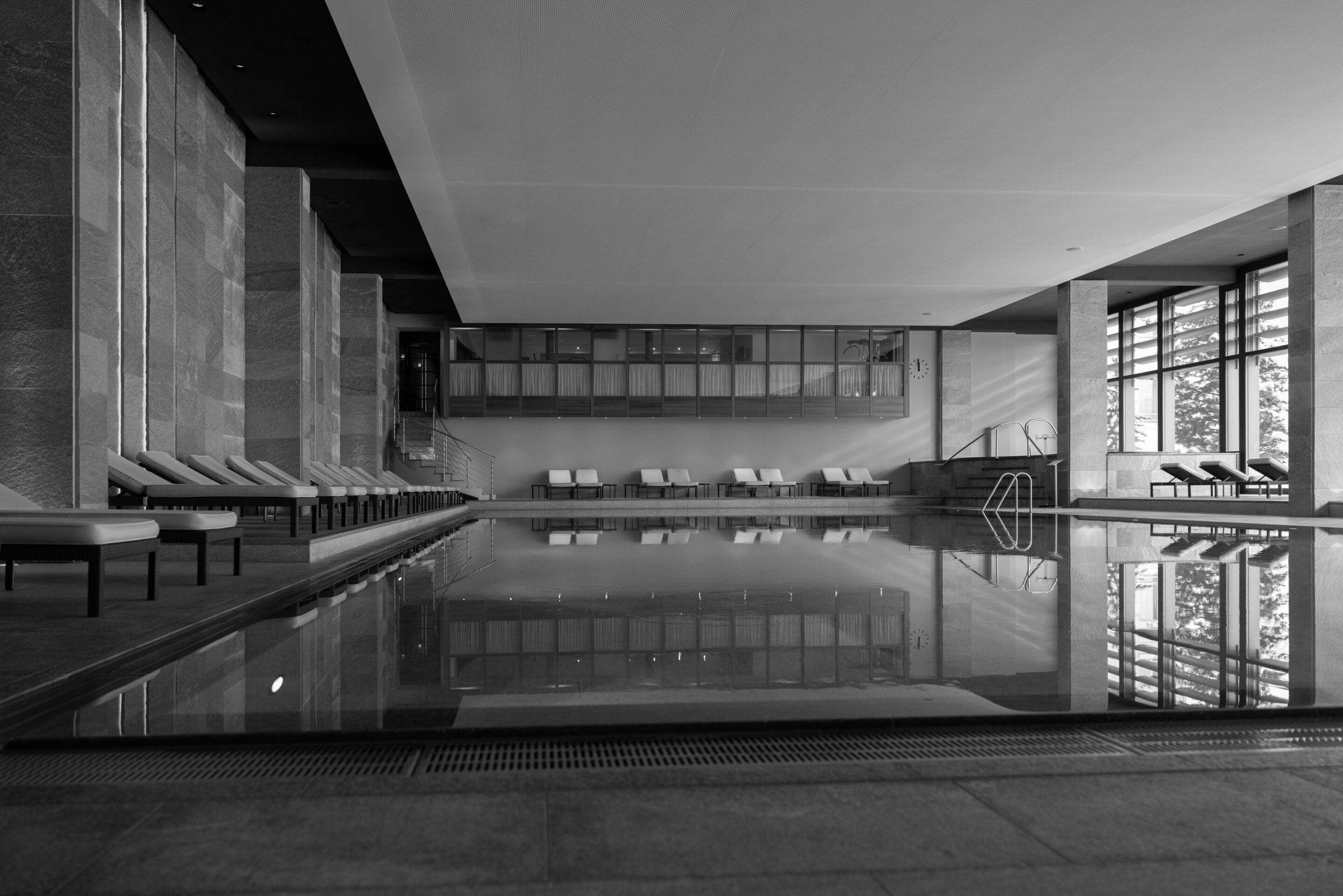 Indoor spa swimming pool with stone walls and panoramic windows, photographed in black and white, Kulm Hotel St. Moritz, St. Moritz, Switzerland
