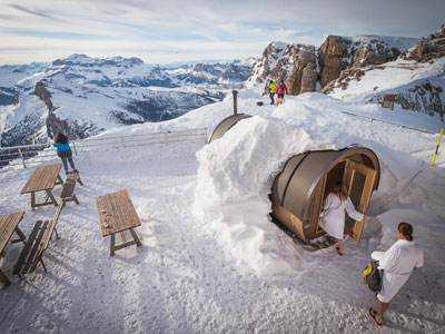 Snow-covered barrel sauna on the refuge terrace with bathrobe-clad guests and mountain views at Rifugio Lagazuoi, Dolomites