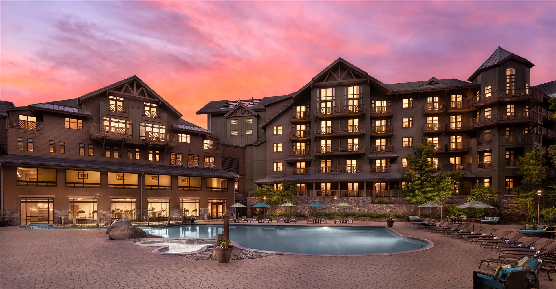 Lodge exterior and terrace glowing at sunset beneath the ski slopes, The Lodge at Spruce Peak, Stowe, USA