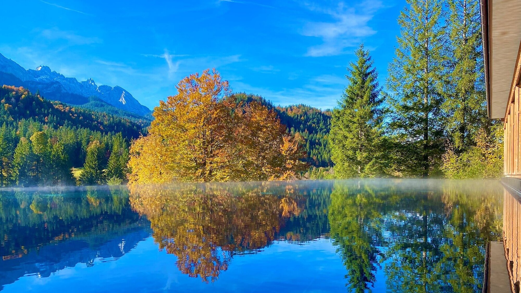 Pool reflecting autumn trees and mountains at Schloss Elmau, Bavarian Alps, Germany