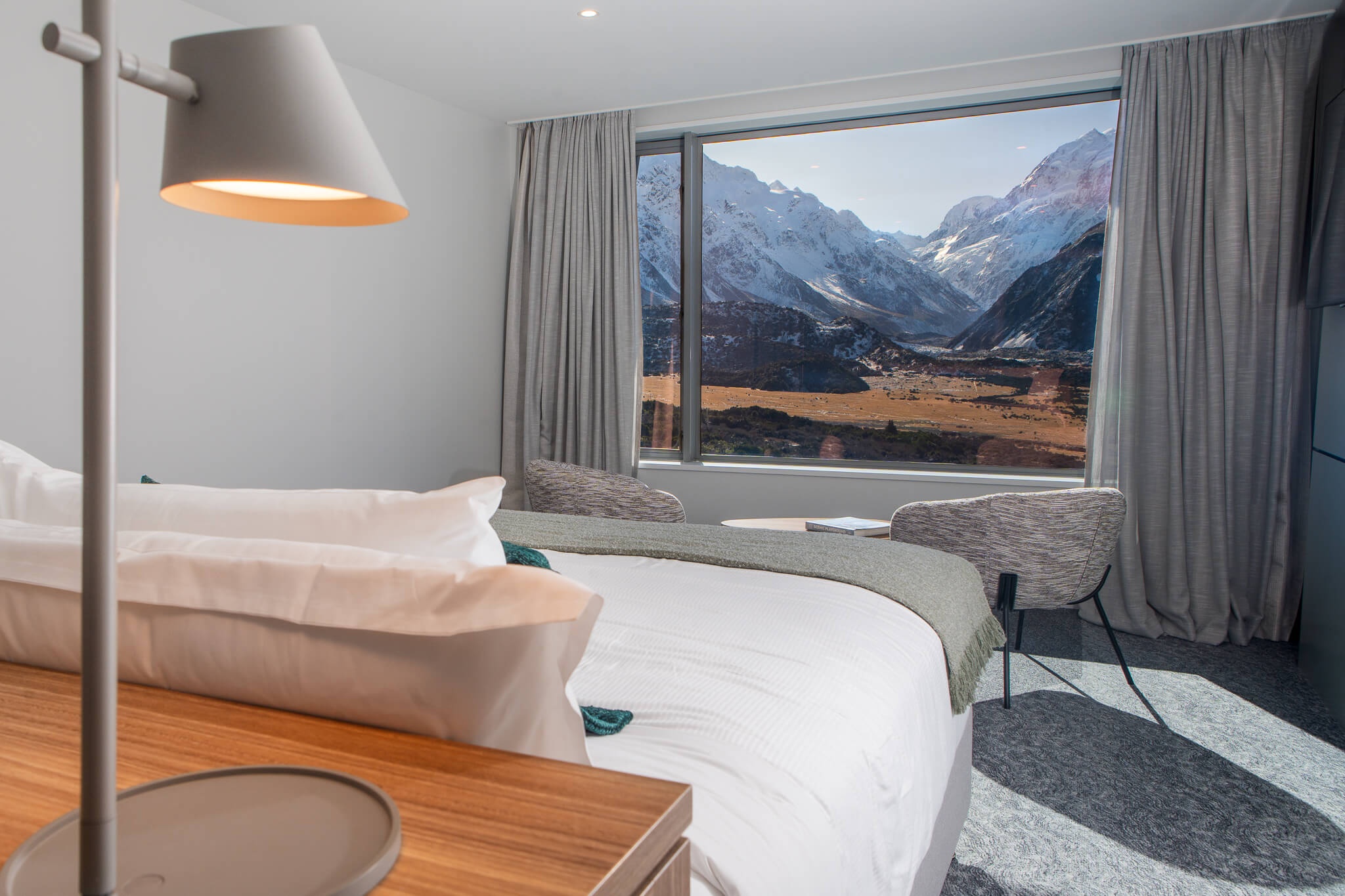 Hotel bedroom with white bedding and a large window framing rugged mountains.
