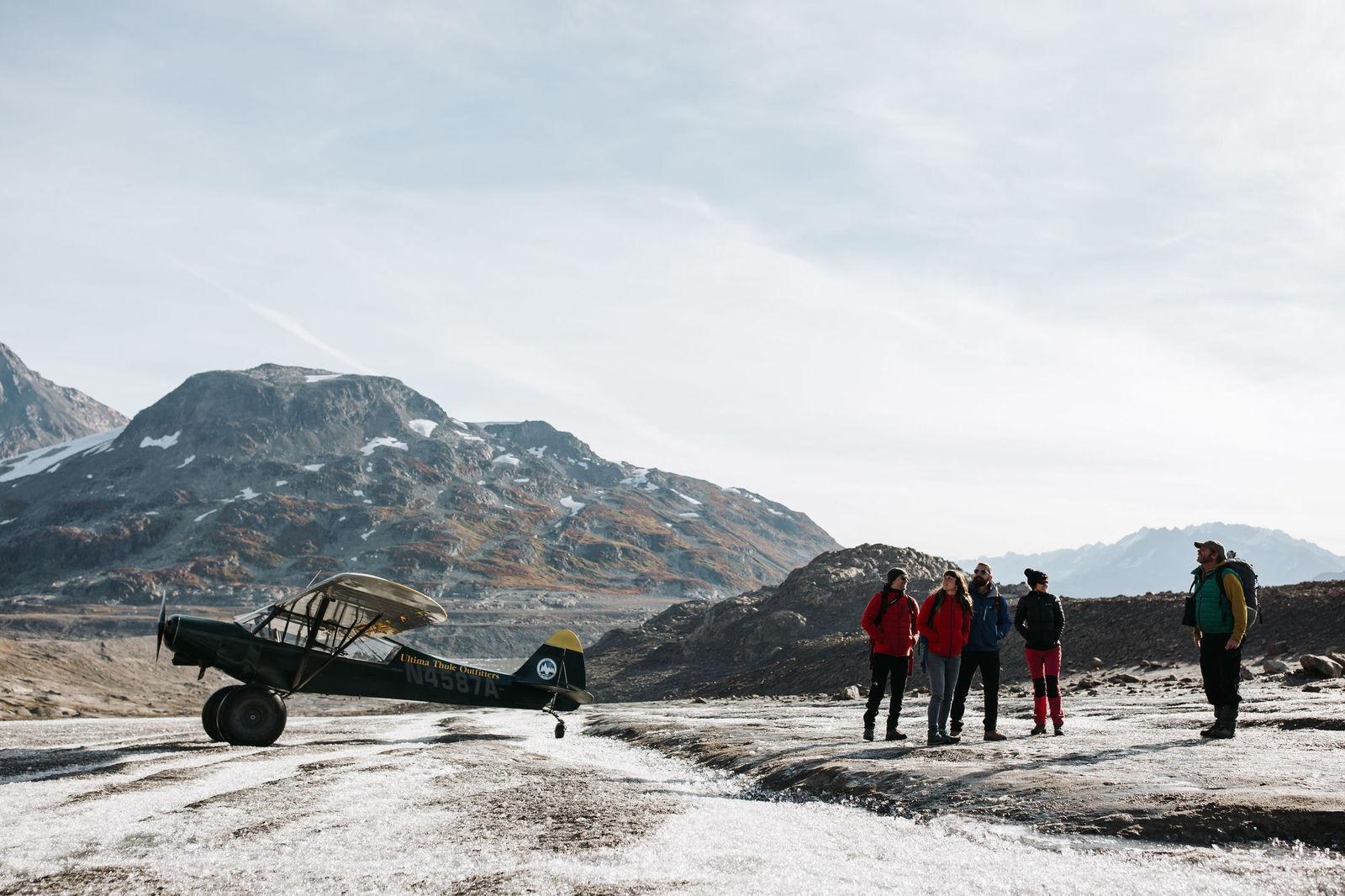 Bush plane and guests on a glacier beneath rocky peaks, Ultima Thule Lodge, Alaska, USA