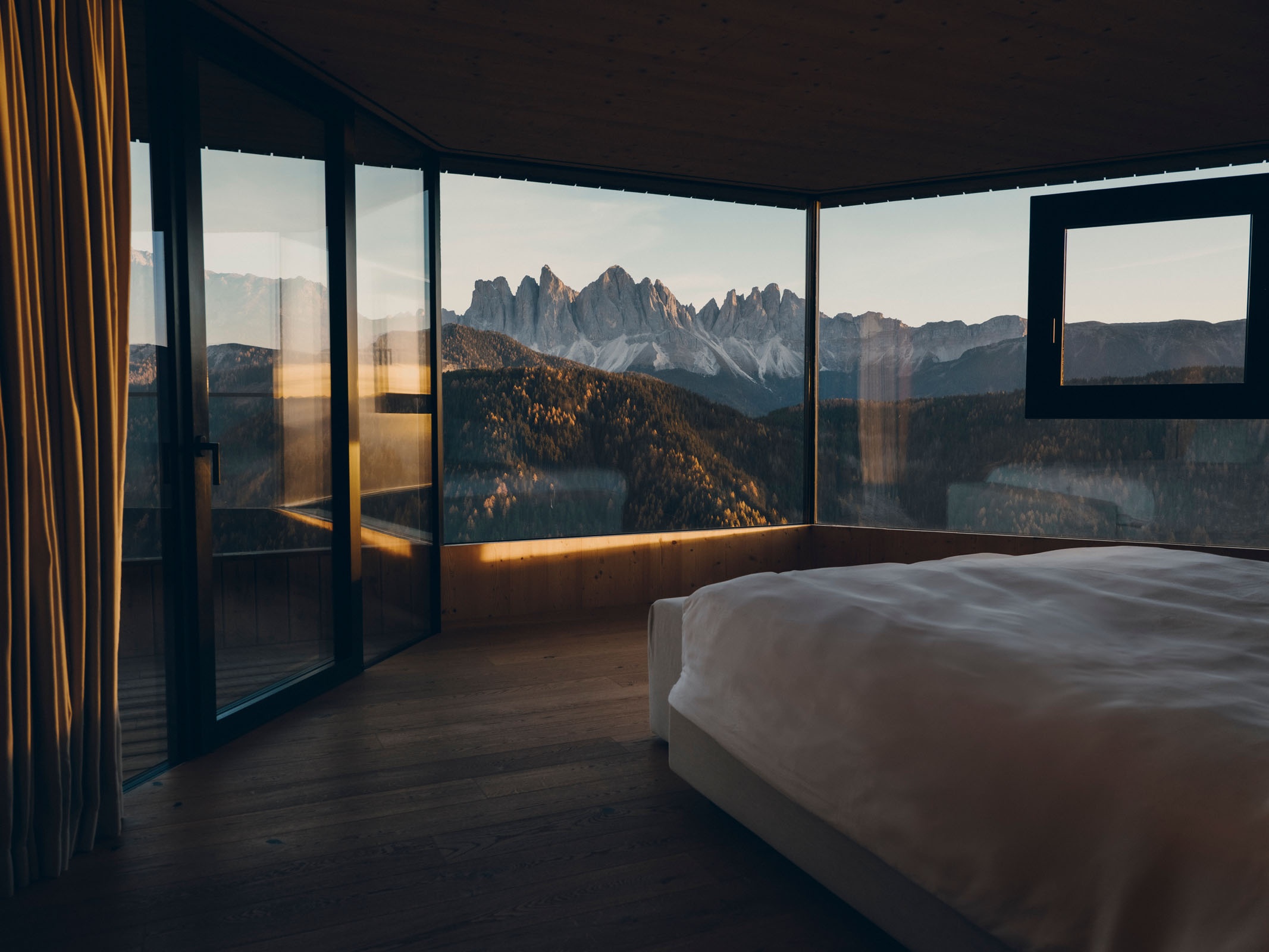 A FORESTIS suite bedroom with a king bed facing floor-to-ceiling windows and mountain views, Dolomites, Italy