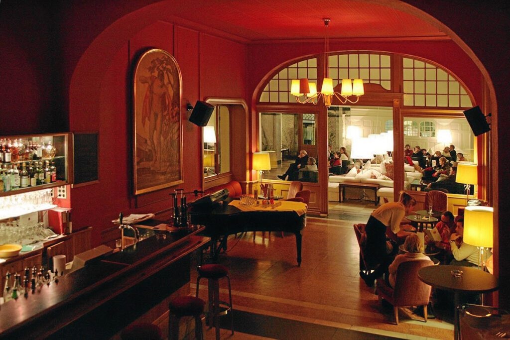 Red-walled Piano Bar with a grand piano, seating and warm lamps at Berghotel Schatzalp, Davos, Switzerland