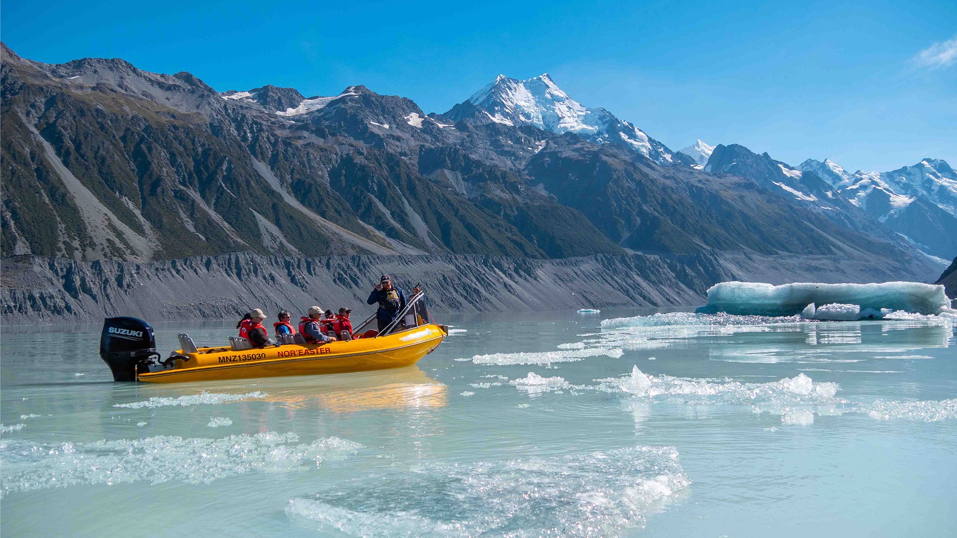 Yellow passenger boat on a glacial lake beside floating ice and mountain slopes at The Hermitage Hotel, Aoraki/Mount Cook