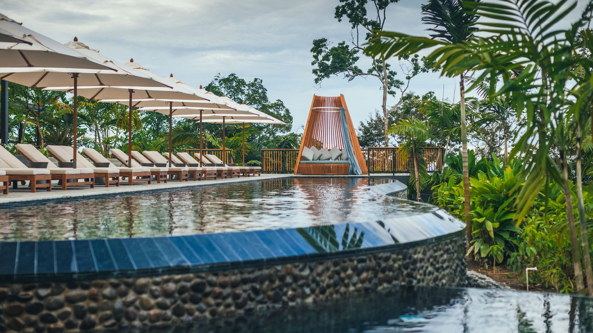 Curved infinity pool lined with loungers and umbrellas, Nayara Tented Camp, Arenal, Costa Rica