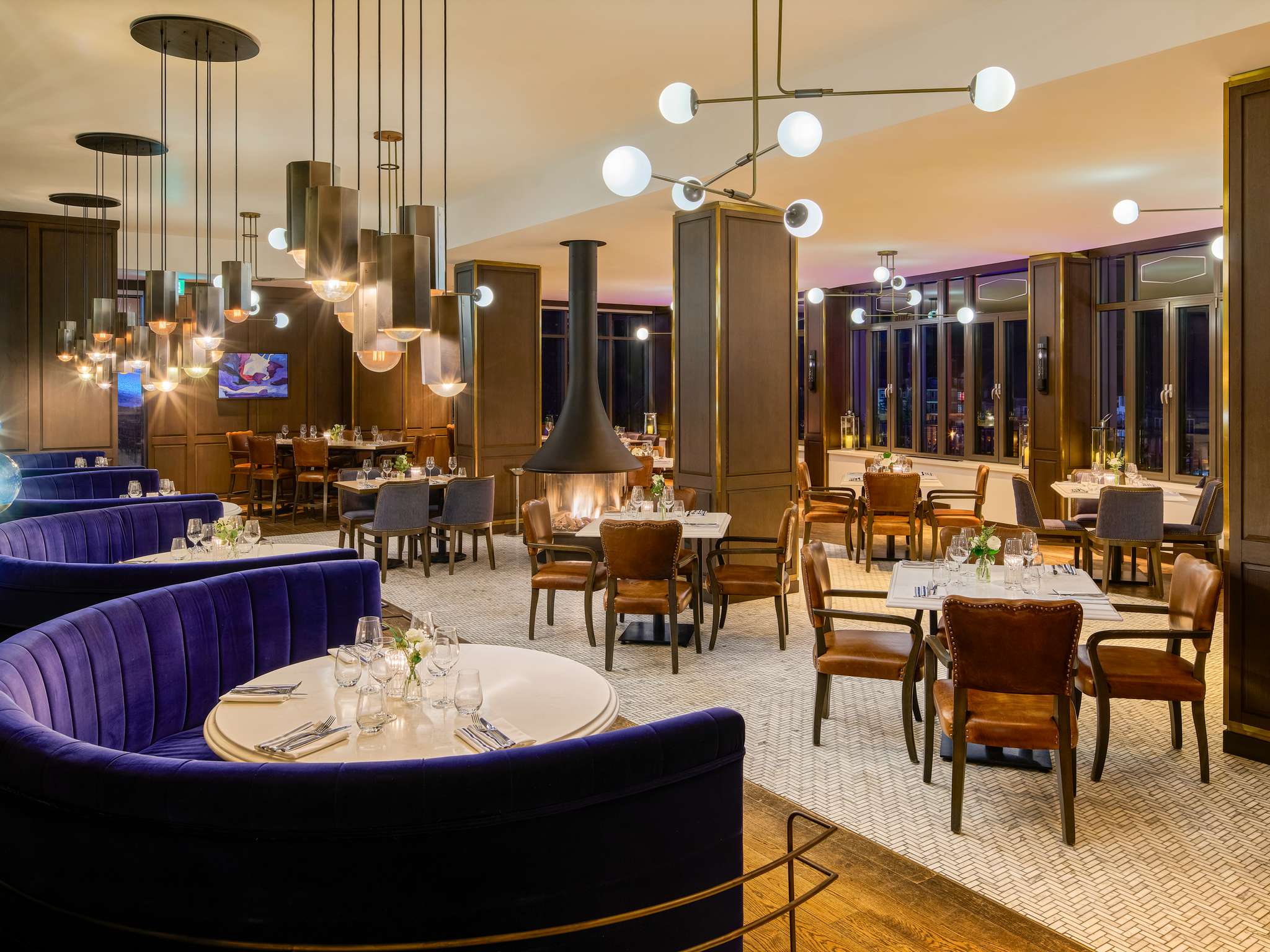 Dining room at Fairmont Tremblant with purple banquettes, round tables and pendant lights.