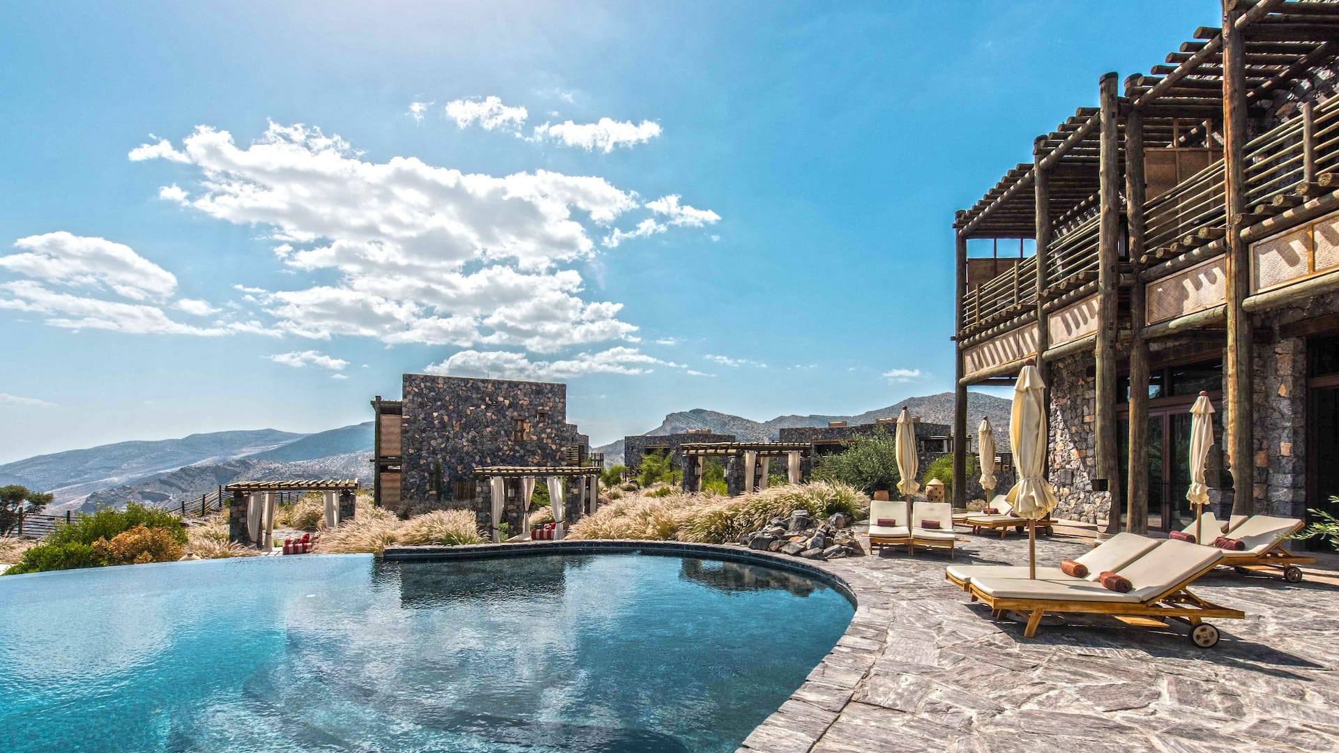 Infinity pool beside stone resort buildings and loungers overlooking the mountains, Alila Jabal Akhdar, Jebel Akhdar, Oman