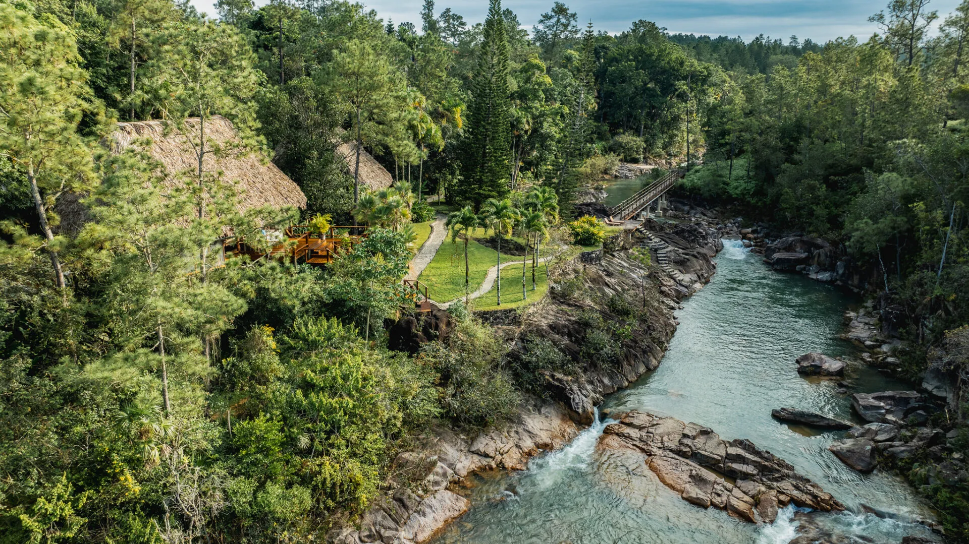 Aerial exterior of riverside thatched cottages in lush forest, Blancaneaux Lodge, Mountain Pine Ridge, Cayo, Belize