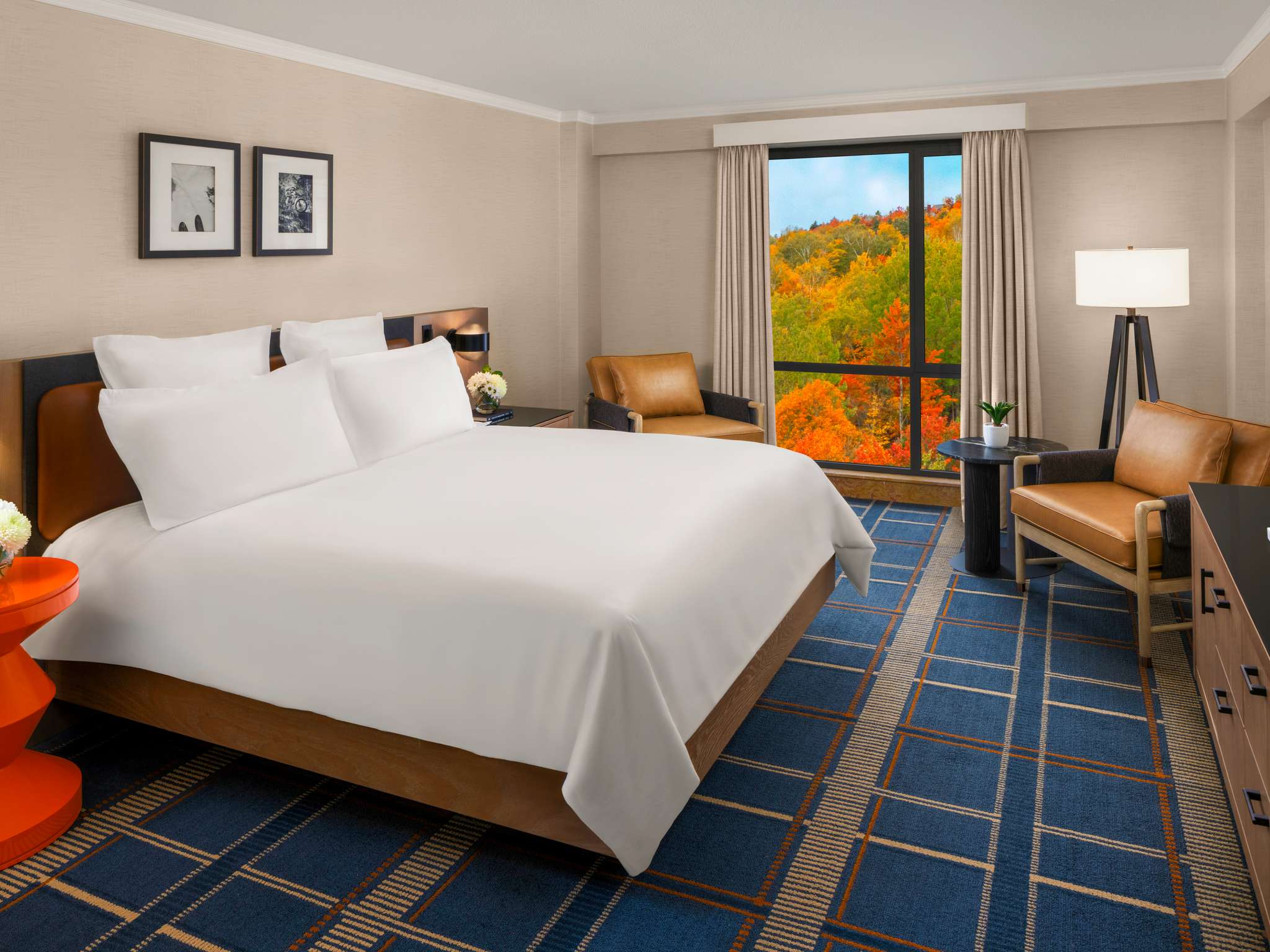 King guest room with white bedding, blue checked carpet and a balcony opening onto autumn foliage at Fairmont Tremblant