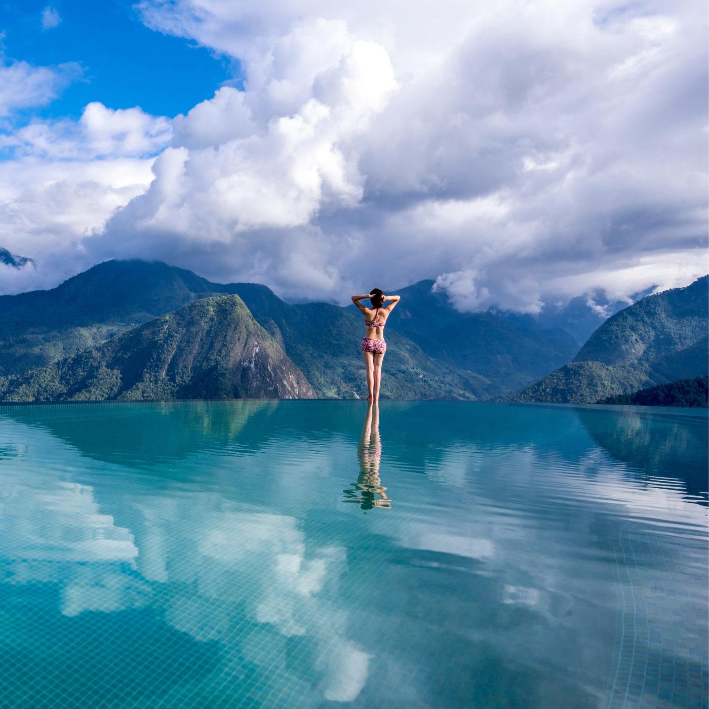 Guest standing in an infinity pool overlooking cloud-wrapped mountains, Topas Ecolodge, Sapa, Vietnam